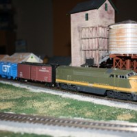 My Canadian Natonal diesel with the green and gold paint in front of my steam coaling tower and water tower. It is on the siding for the lumber company.