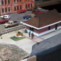 FINISHED STATION AND PARKING LOT WITH A CARDBOARD MOCK-UP OF THE JANION BUILDING BEHIND. THE JANION WAS ORIGINALLY BUILT AS A HOTEL, THEN A WAREHOUSE, ASSAYER'S OFFICE, COLD STORAGE FACILITY, BOTTLING PLANT FOR PACIFIC BEER, OFFICE OF THE LAKE OF THE WOODS MILLING COMPANY, AND THEN BECAME HEADQUARTERS OF THE E&N RAILWAY. IT HAS SAT VACANT FOR 35 YEARS.